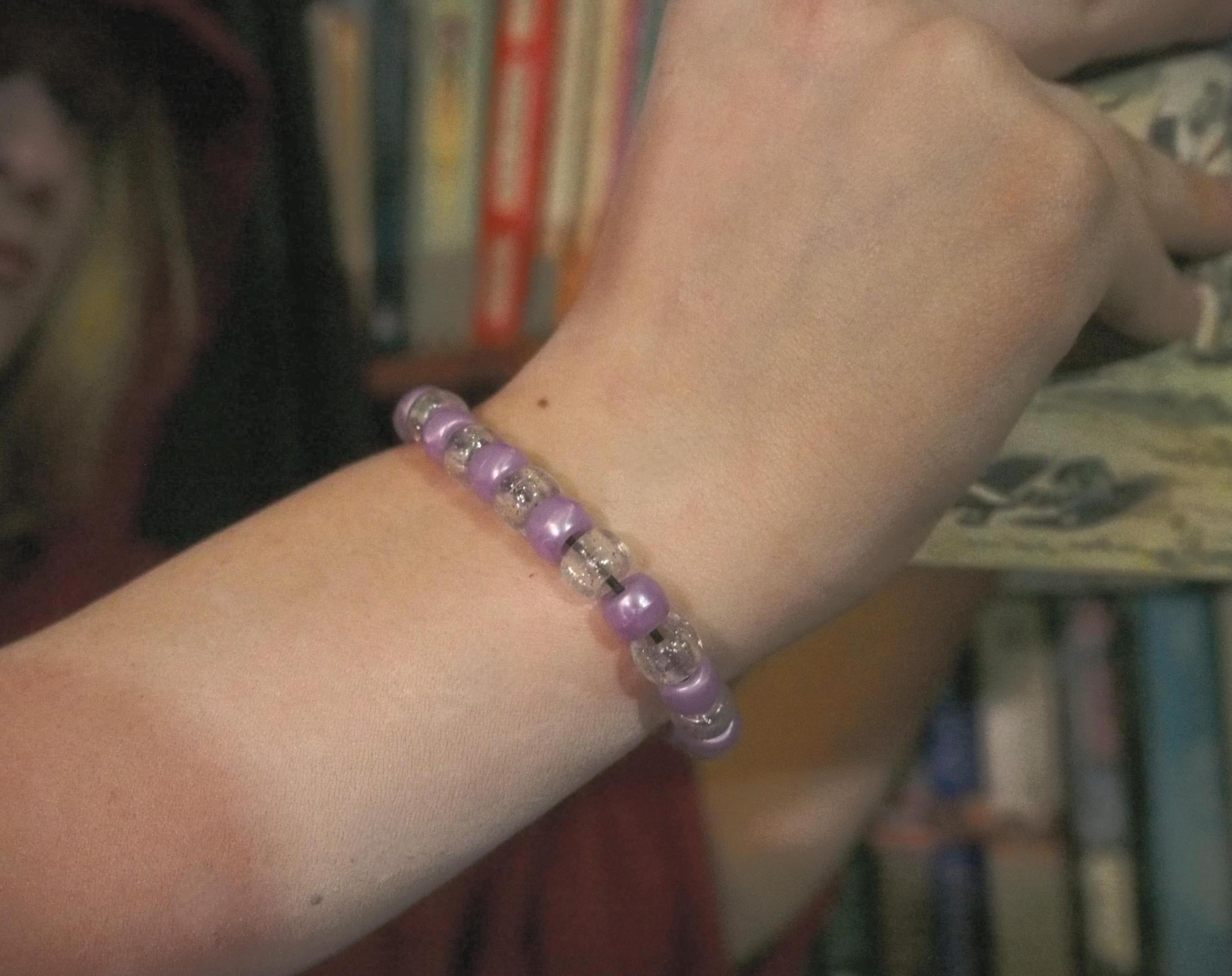 Close-up of a wrist wearing a purple beaded bracelet with a blurred background