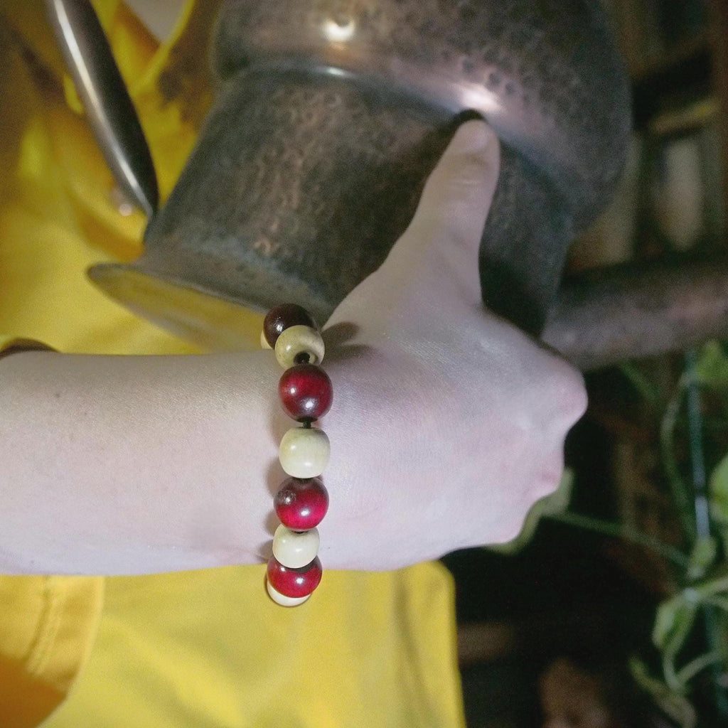 Close-up of a hand wearing a bracelet with red and beige beads, holding a metal cup.