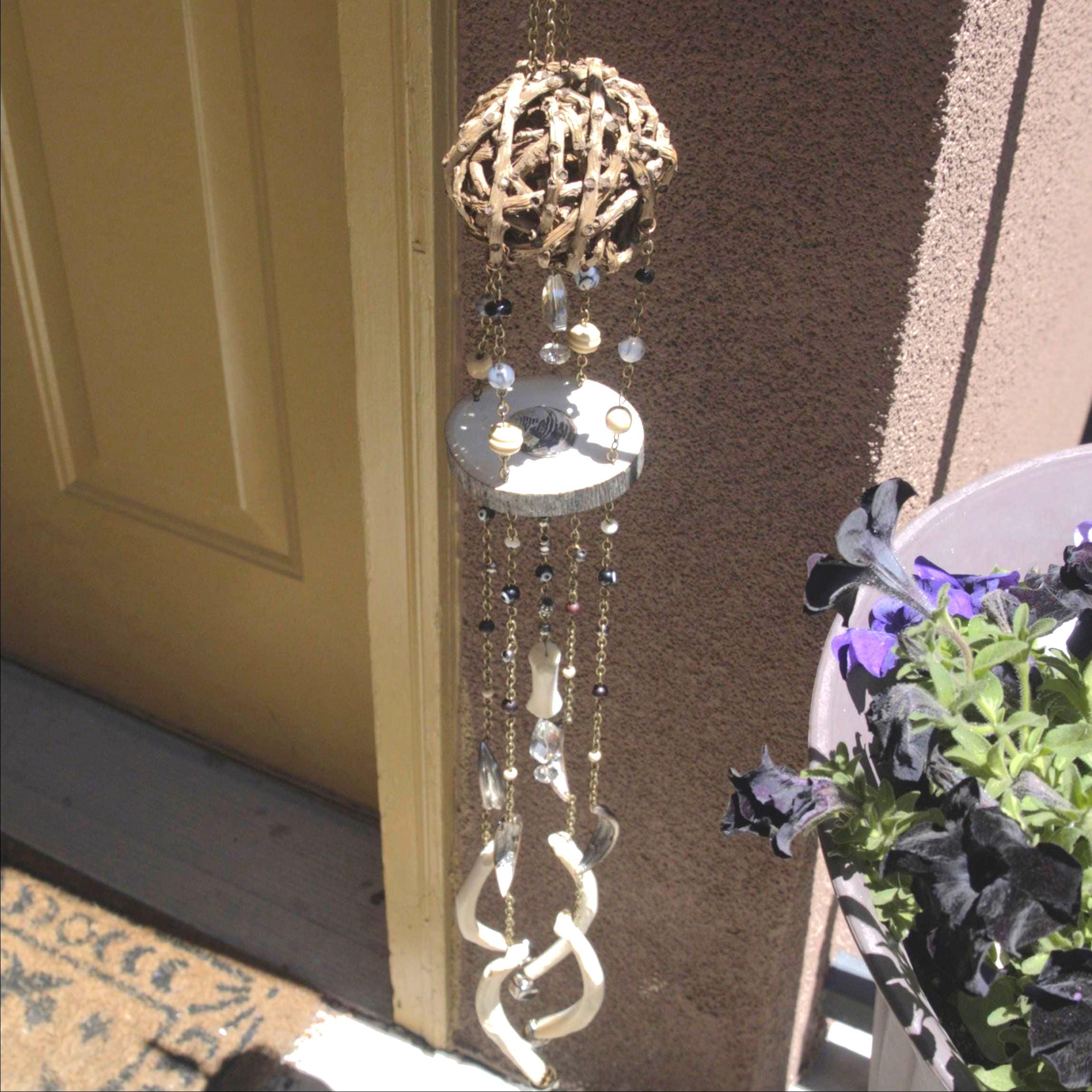 Decorative wind chime hanging on a door with a plant in the foreground