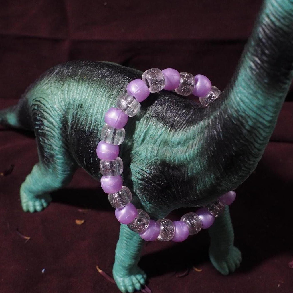 Plastic dinosaur toy with a purple beaded necklace on a dark background