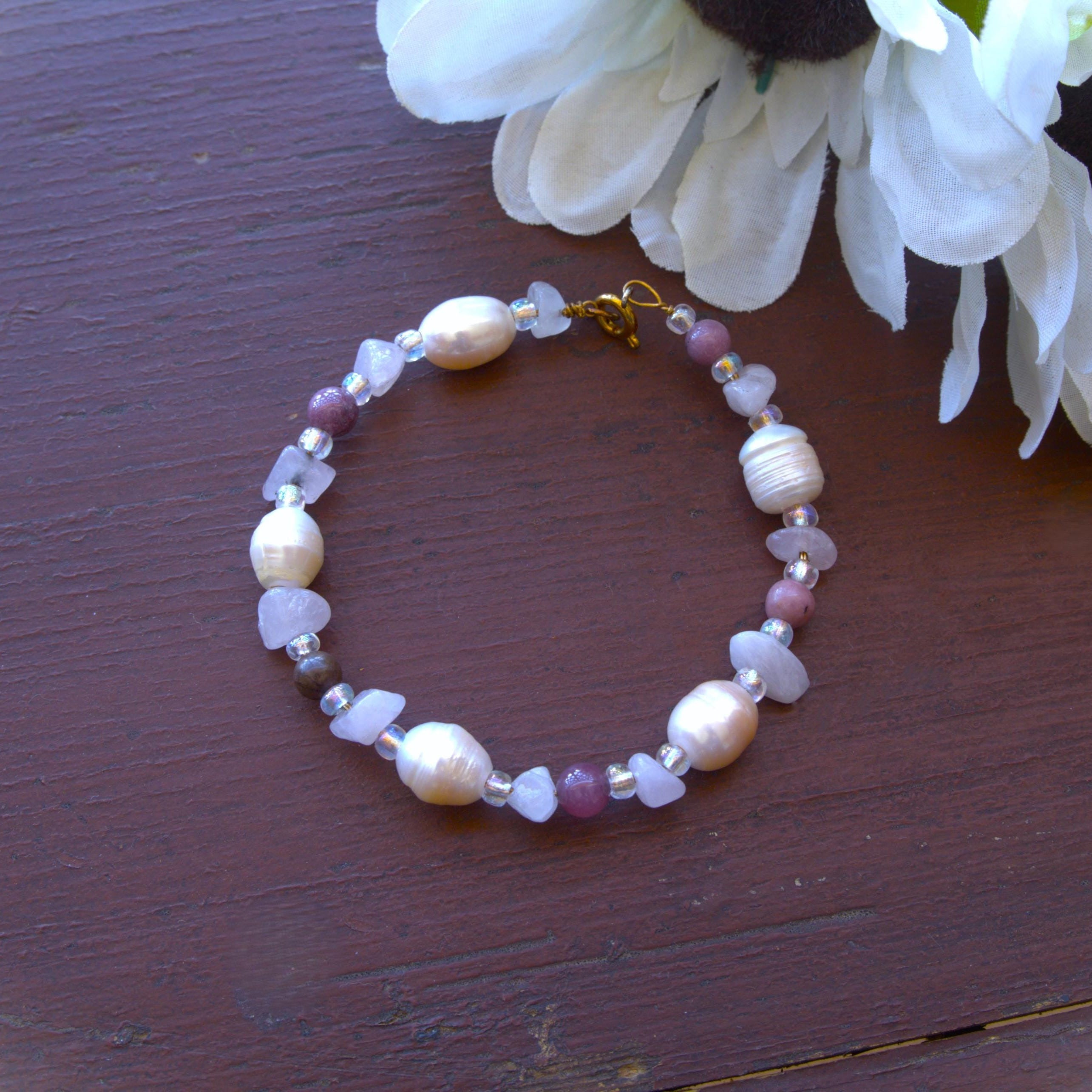 Beaded bracelet with pearls and gemstones on a wooden surface with a white flower.