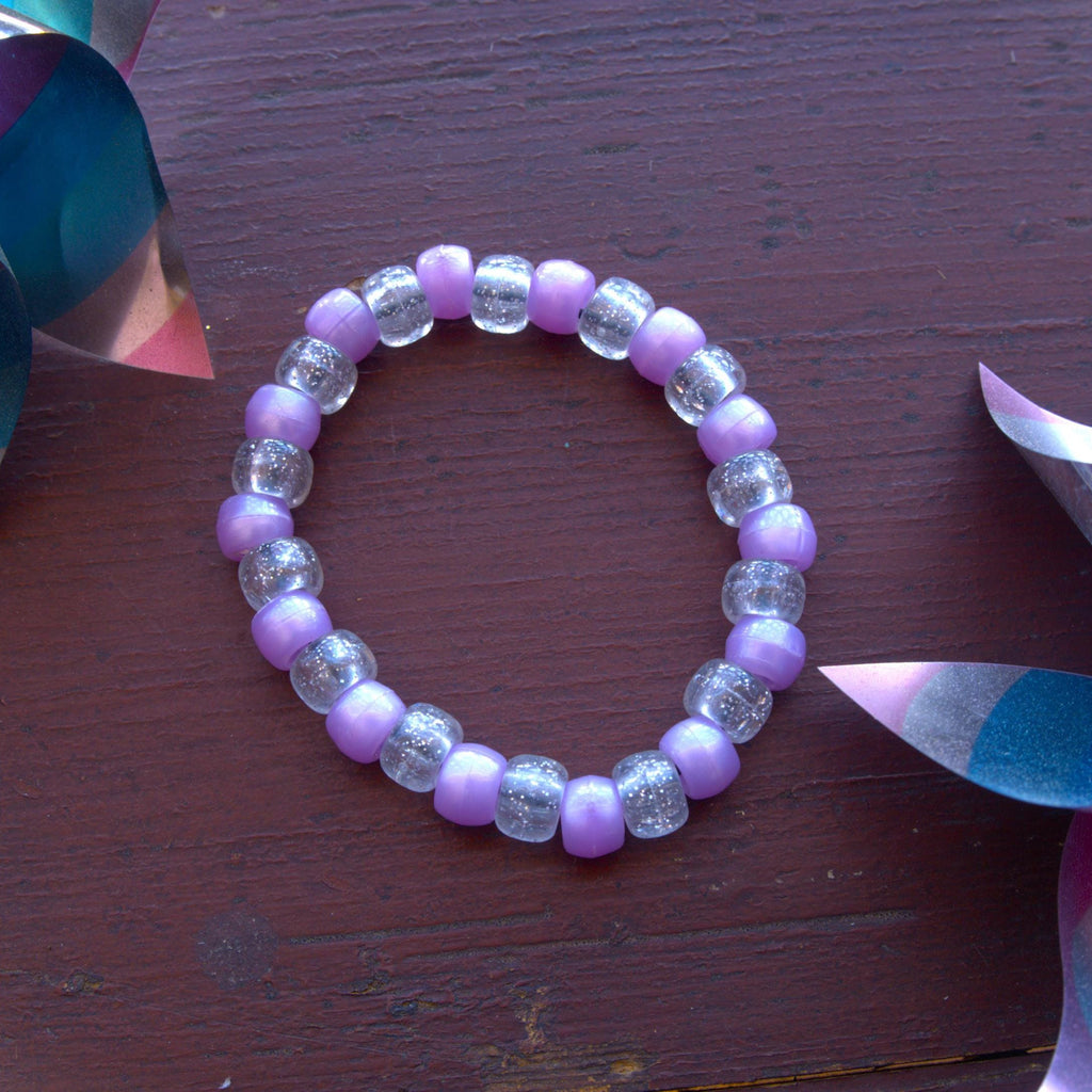 Purple beaded bracelet on a wooden surface with colorful objects around