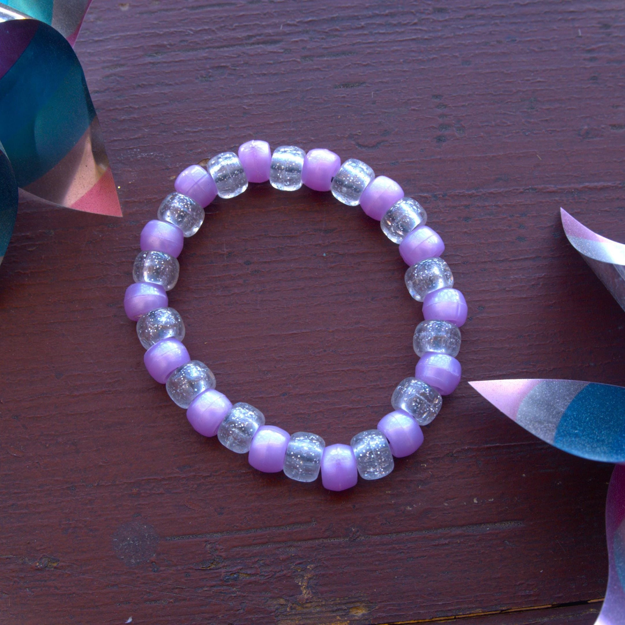 Purple beaded bracelet on a wooden surface with colorful objects around